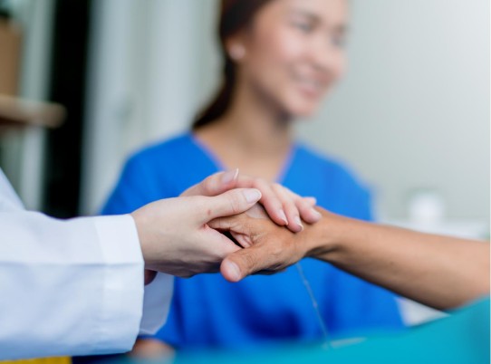 two hands holding each other with a nurse in the background